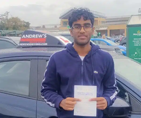 Ramija Abeysighe holding his driving test pass certificate beside an Andrew’s Driving School car after passing first time in Rhyl with Mark Bilton
