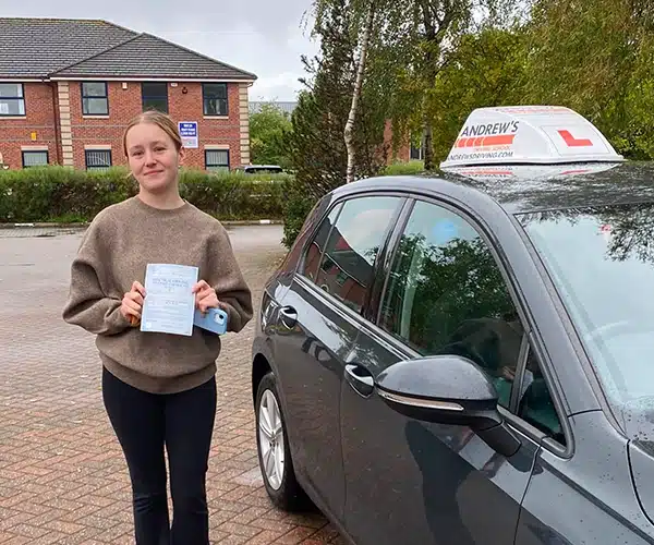 
Amber Parry holding her pass certificate beside instructor Andy Williams’s Volkswagen Golf after passing her driving test at Chester Test Centre.