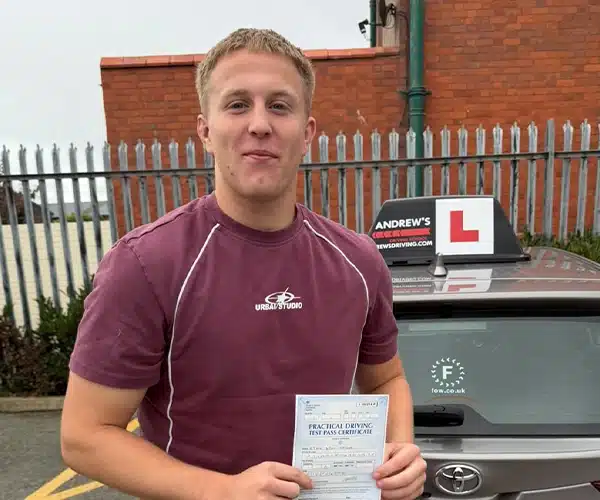 

Cian Taylor holding his pass certificate at Rhyl Driving Test Centre beside Ursula Cowie’s Andrew’s Driving School tuition car after passing first time with three minor faults.