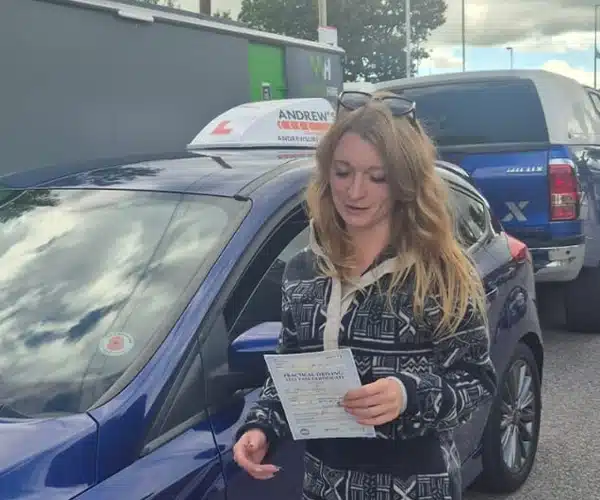 
Heidi Hughes holding her driving test pass certificate beside Craig’s Andrew’s Driving School car in Wrexham.