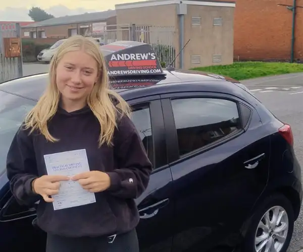 Millie holding her pass certificate beside instructor Mark Bilton’s purple Mazda outside Rhyl Driving Test Centre.